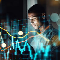 A young man looking at a digital screen with stock market visualized on it
