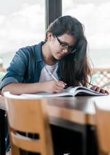 Student sitting at a table, reading a book