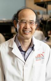 A man in a white lab coat smiles at the camera